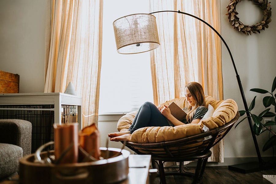 Girl in a green shirt and jeans sitting in a round chair with a hanging lamp and other functional and comfortable furniture in Rochester, IL.