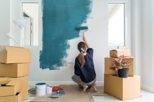 Woman in a blue top using a roller brush with teal paint color to paint her living room walls in Petersburg, IL