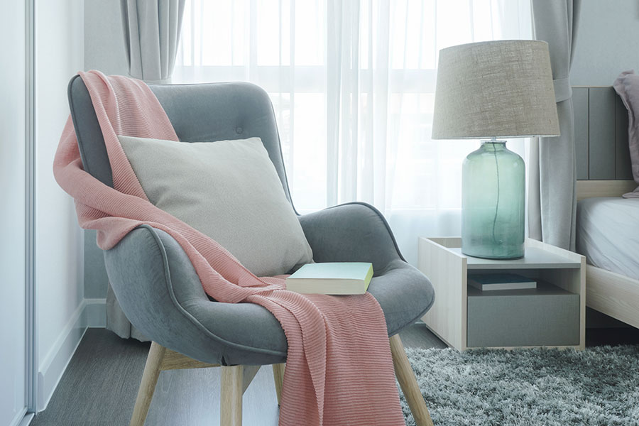 A gray armchair in a residential bedroom in Springfield, IL, with a pink blanket and white pillow used for modern design.